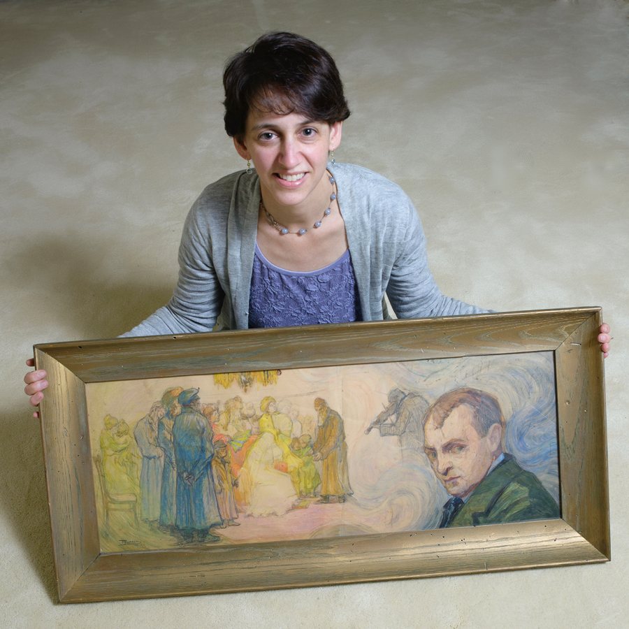 Elizabeth Rynecki '91 poses with a painting by her great-grandfather Moshe Rynecki — a self-portrait that situates the artist beside, but not part of, a wedding ceremony. (Shoey Sindel Photography)