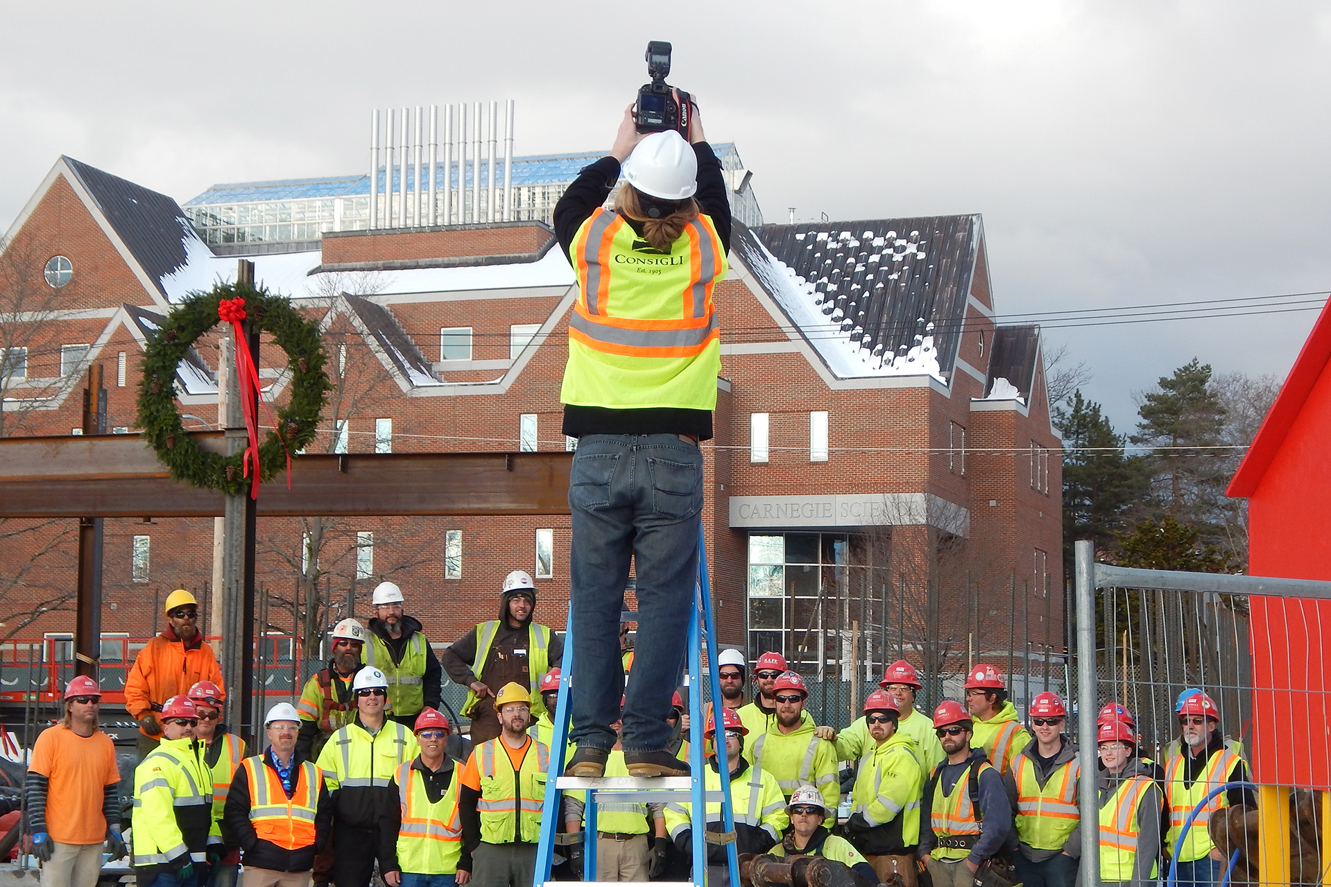 Multimedia producer Theophil Syslo puts the Campus Construction Update ladder to good use on Dec. 5 as he photographs a wreath and workers at the Bonney Science Center. The image was presented to Michael Bonney '80 and Alison Grott Bonney '80, whose family foundation made a gift that is anchoring the building project. (Doug Hubley/Bates College)