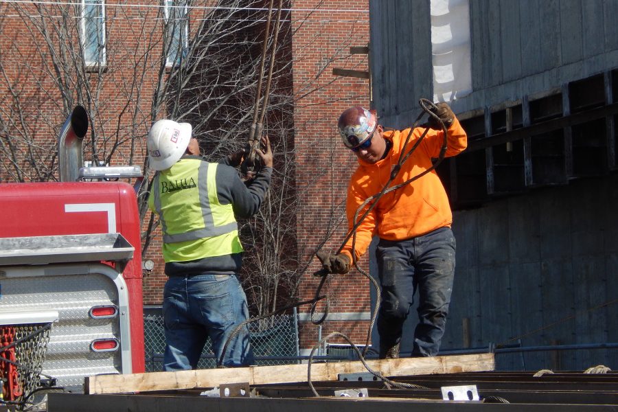 Steel workers delivering a load of structural components on March 3 prepare to attach the next load to the crane cables. (Doug Hubley/Bates College)