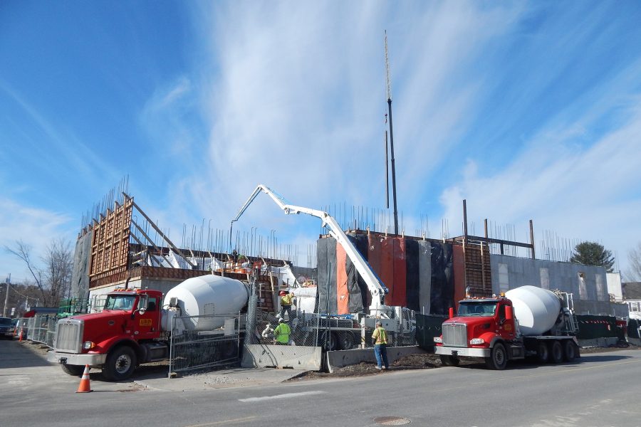 With the next load already lined up, the pumper at center sends concrete through the boom clear across the Bonney center footprint to build a wall on the far side. Meanwhile, new steel dangles over the building from a crane. (Doug Hubley/Bates College)