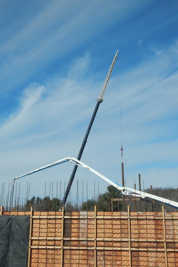 Entering from the right, the limber boom of a concrete pump hovers over a new wall placement on the south side of the Bonney center while a crane hoists steel up to the second floor. (Doug Hubley/Bates College)