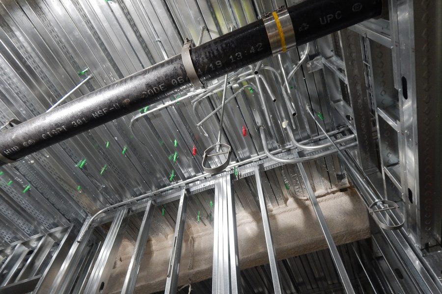 A drainpipe crosses over a room in the Bonney center basement. The green and red objects in the ceiling deck are Bang-Its, grommets that provide access for utility connections through the concrete floor slab above. (Doug Hubley/Bates College)