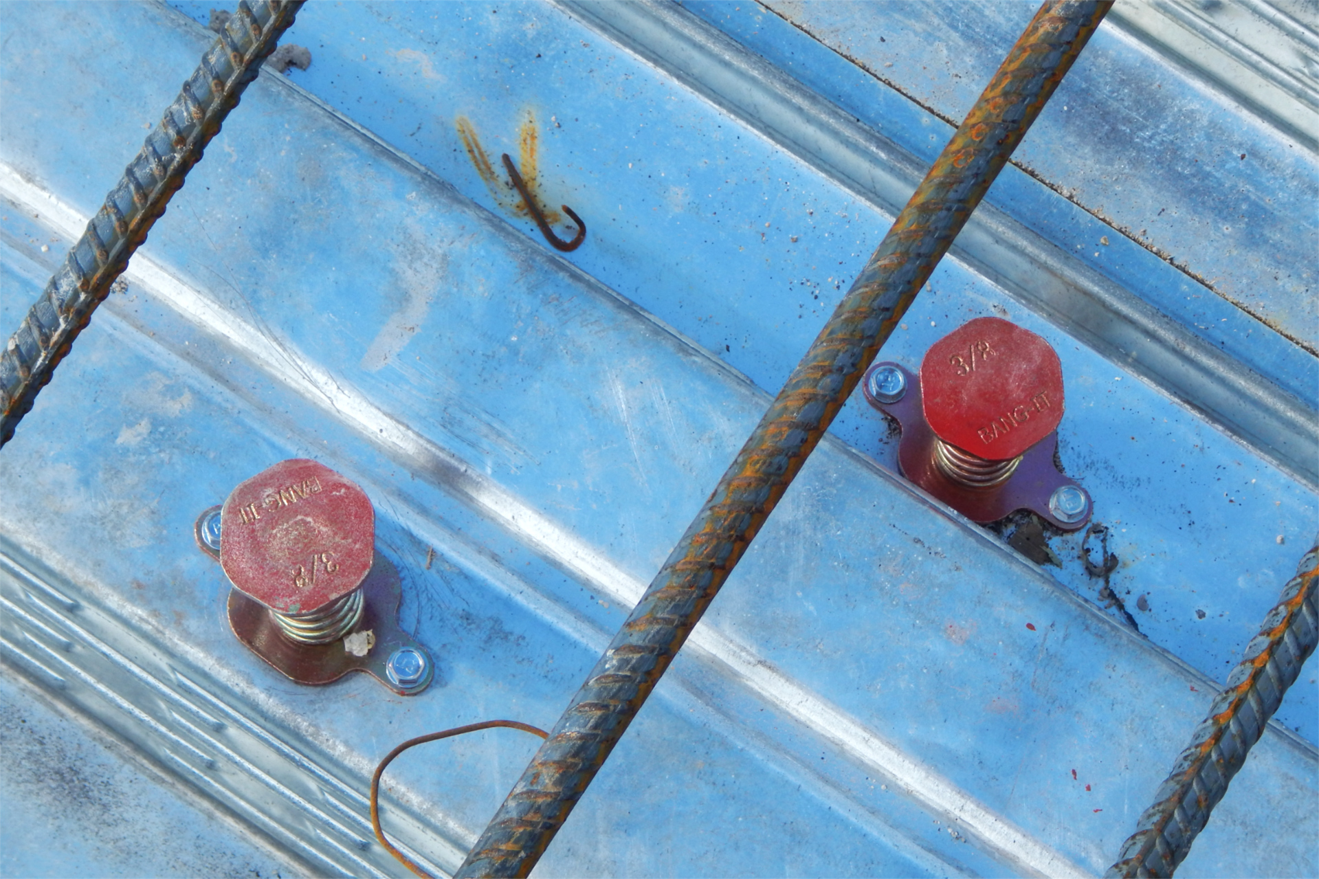 The red caps belong to Bang-Its. Used to both mark future utility installations and provide a fastening point for them, Bang-Its are inserted through holes in the decking before concrete is placed, and are seated by a blow (hence the product name) from one’s boot or a hammer. (Doug Hubley/Bates College)