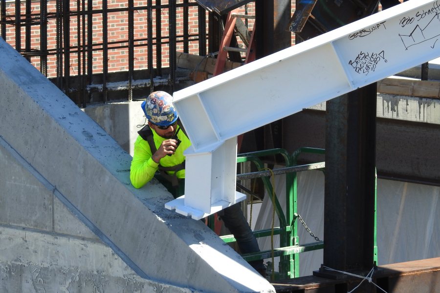 A steelworker uses a pin to line up holes and bolts to fix the beam in place at one end. (Jay Burns/Bates College)