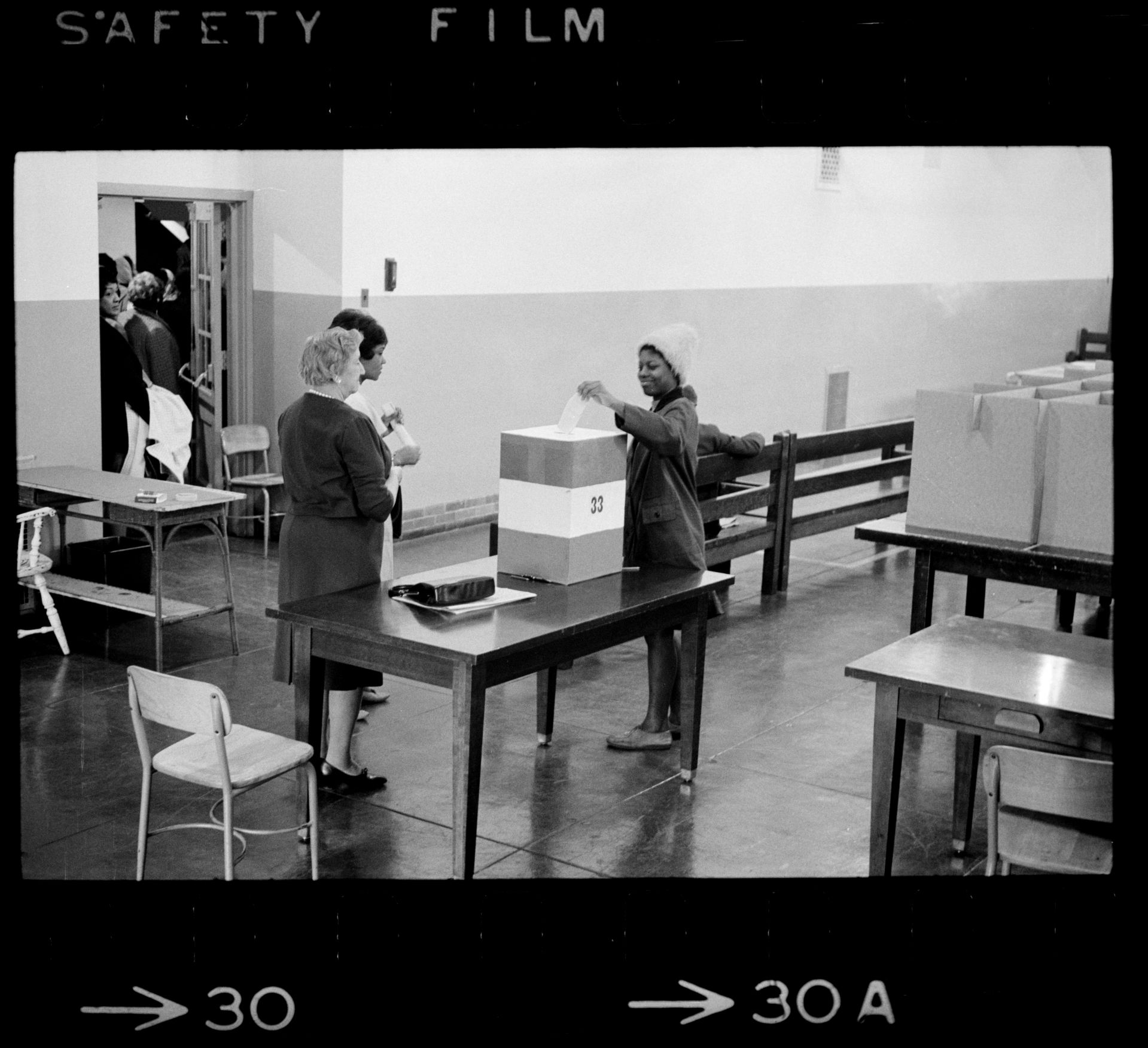 Negro voting in Cardoza [i.e., Cardozo] High School in [Washington,] D.C. / [MST].SummaryPhotograph showing a young African American woman casting her ballot.Trikosko, Marion S, photographer. Negro voting in Cardoza i.e., Cardozo High School in Washington, D.C. / MST. Washington D.C, 1964. Nov. 3. Photograph. https://www.loc.gov/item/2003688167/.