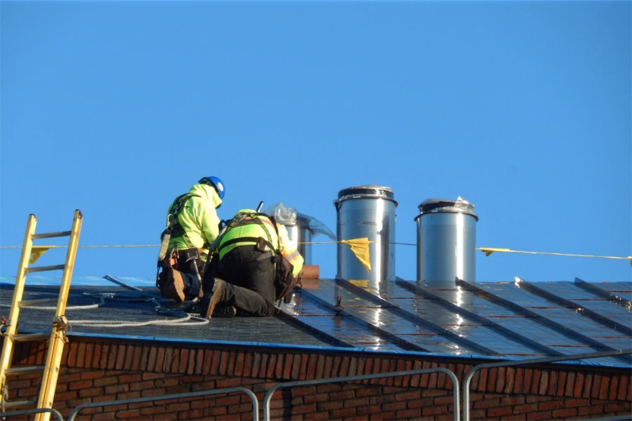 Hahnel Brothers employees place Revere ContinentalBronze roofing panels, at right, on the southeast corner of the Bonney building. Nearby are exhaust stacks for boilers in the penthouse. (Doug Hubley/Bates College)