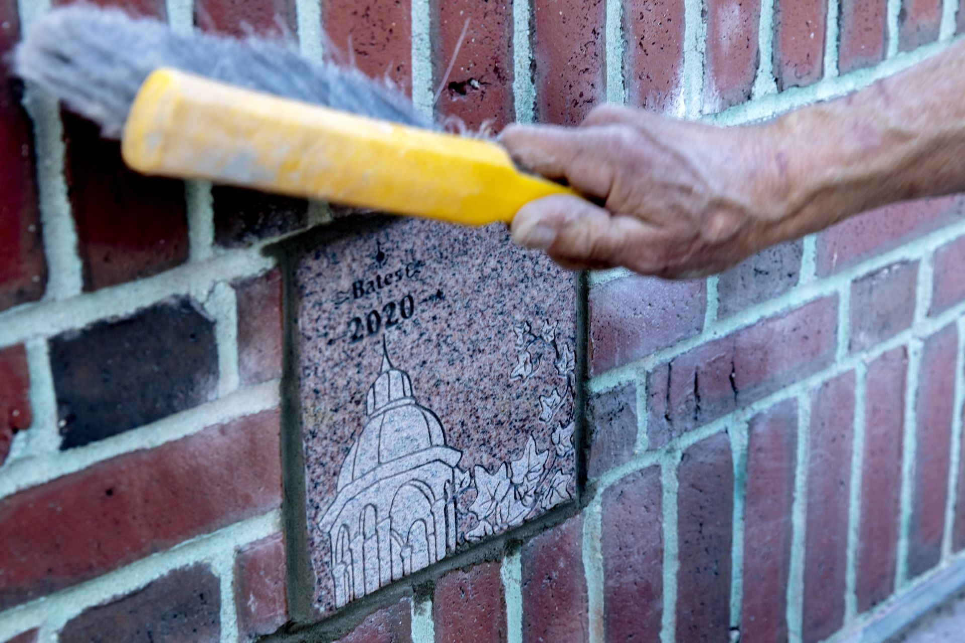 Ron Tardif, mason for facility services, installs the Class of 2020 ivy stone on the front of Pettentill Hall, to the right of the building's entrance.