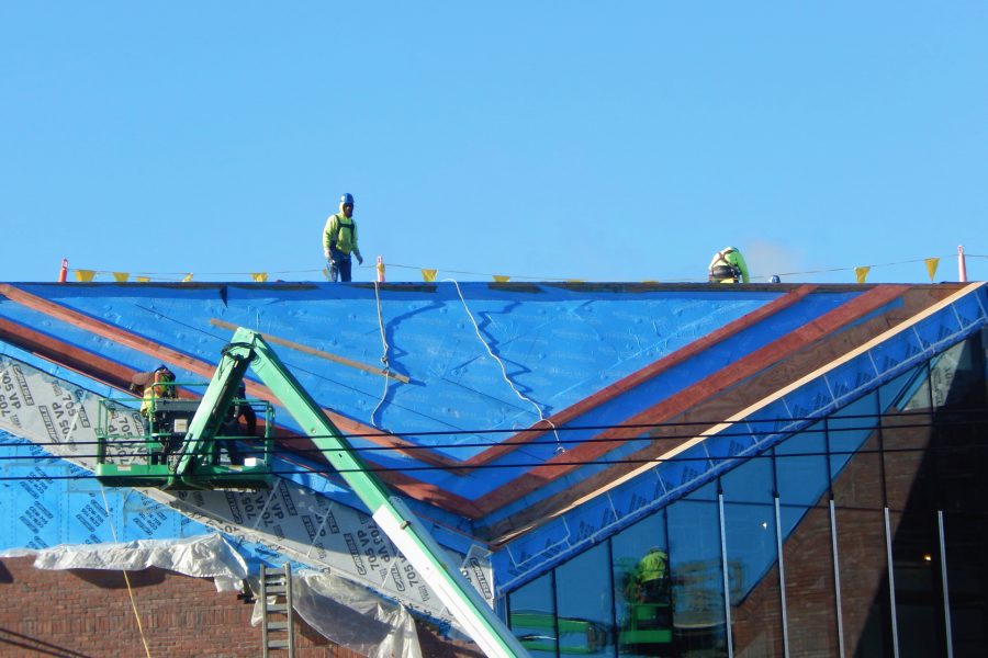 Roofers for Hahnel Brothers are working on the north roof of the Bonney Science Center on March 22, 2021. A second manlift beyond the right edge of the image is reflected in the glass curtain wall. (Doug Hubley/Bates College)