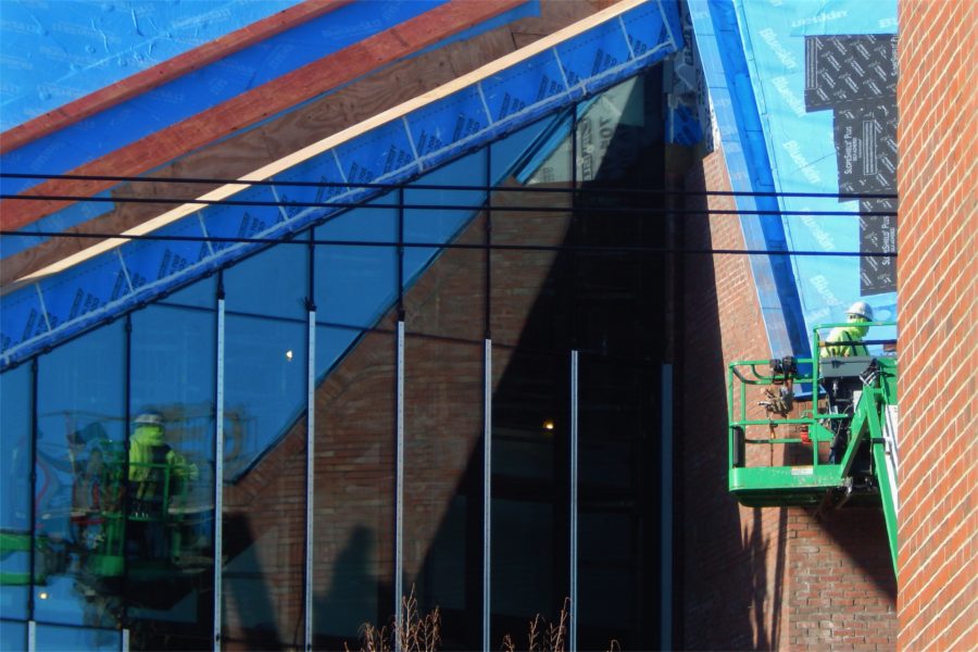 A roofer working in the lift at right has his back to his own reflection, at left, appearing in the Monumental Stair curtain wall.  (Doug Hubley/Bates College)