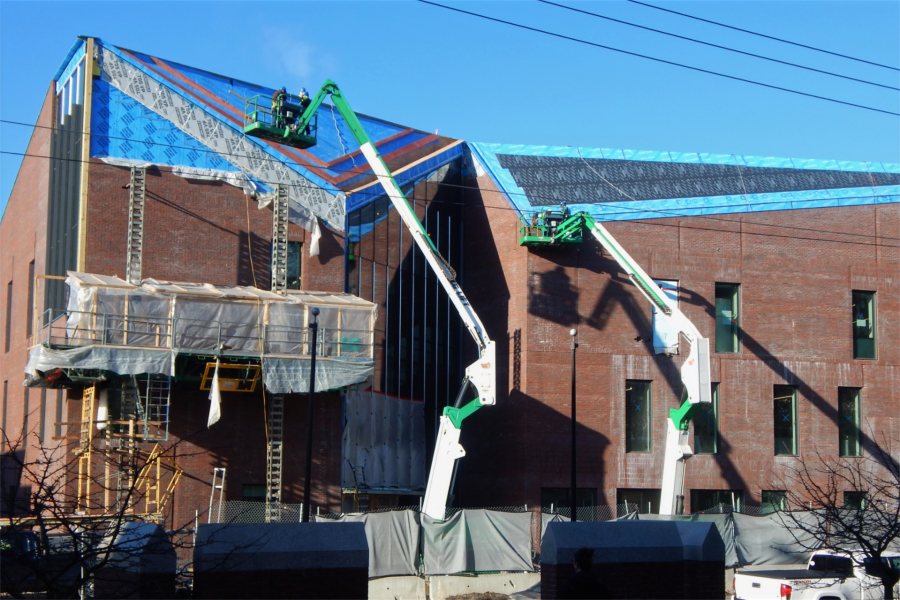 The corner of the Bonney Center at Campus Avenue and Bardwell Street remains the focus of activity on the exterior on March 22. Staging for bricklayers appears at left. The lifts are carrying roofers. Six panes of glass in the Monumental Stair curtain wall, at center, will remain uninstalled until work on the stairway itself is close to finished. (Doug Hubley/Bates College)