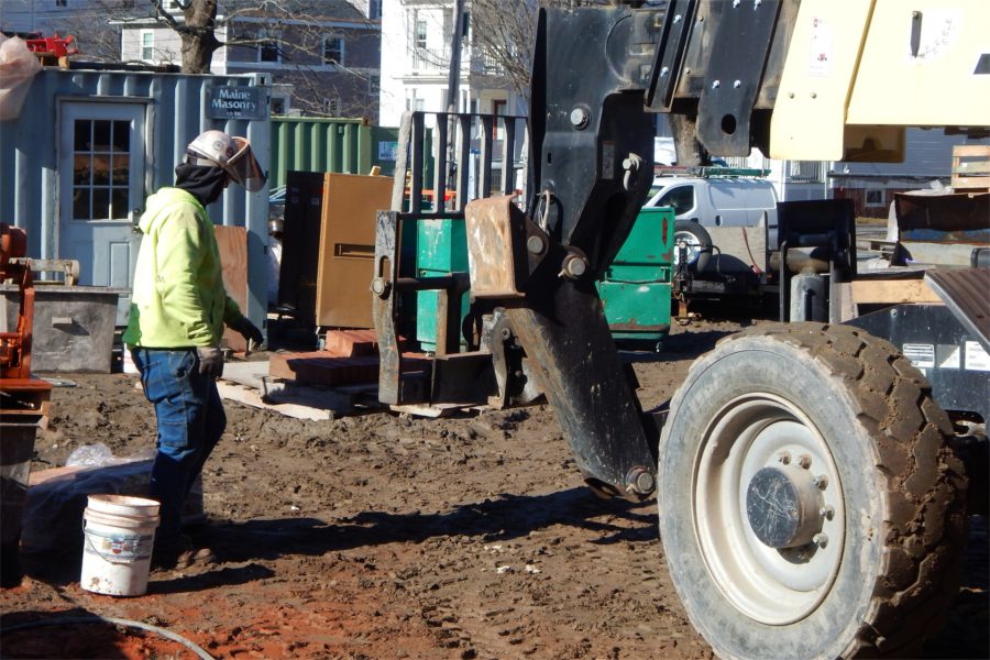 A mason’s tender watches as a forklift gets underway with a load of bricks bound for the Nichols Street side of the Bonney Science Center. Note the red patches on the ground at lower left where dust from cutting bricks has fallen. (Doug Hubley/Bates College)