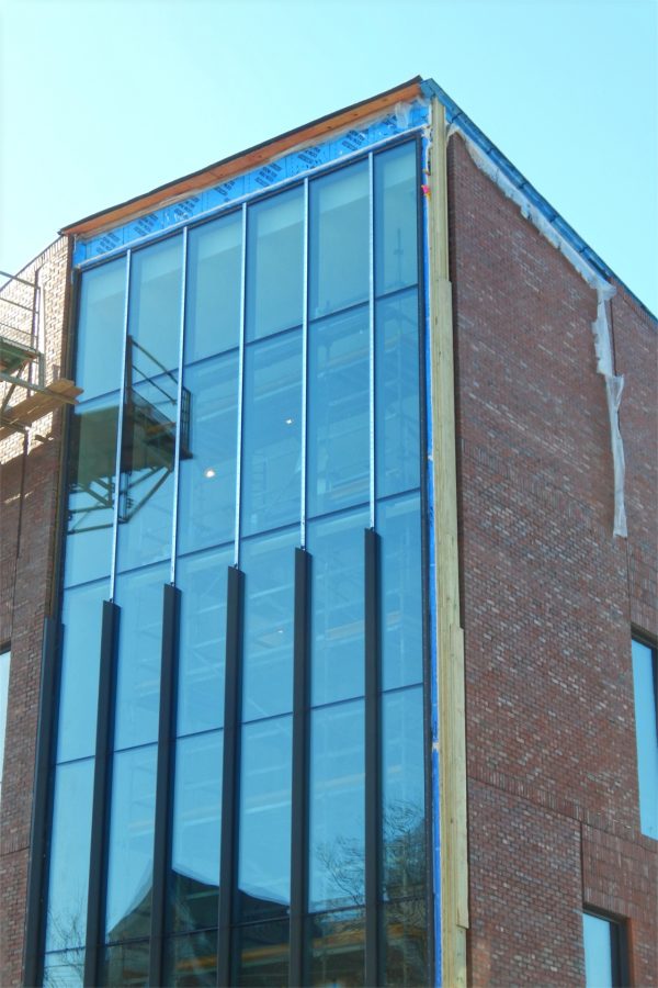 Installation has begun of "snap caps," the decorative vanes shown on the lower section of the glass wall called the Beacon, facing Campus Avenue and the Historic Quad. (Doug Hubley/Bates College)