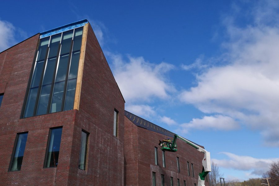 Roofers in a lift are about to apply trim to a section of the Bonney Science Center roof overlooking Campus Avenue on April 26, 2021. (Doug Hubley/Bates College)