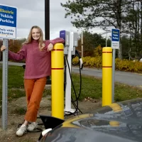 Ecorep Tamsin Stringer ’22 of Bloomington, Ind., poses at the new electric charger stations behind Underhill in the Merrill Gym parking lot.“Underhill Electric Vehicle Chargers Project “Bates has installed other EV chargers in the past. This project will be different for three primary reasons. First, we have already received a grant from CMP for the make-ready infrastructure portion of the project, which has historically been the bulk of the expenses for EV charger installations. Secondly, this project will include installing level 2 chargers for the first time at Bates, which will allow for monetary collections for charging, tiered charging for different kinds of customers, and incentivize to move one’s car once it's fully charged. Finally, this project allows for future EV charger installations in the same location for much lower cost, because the make-ready infrastructure for more EV chargers will be easily accessible.
