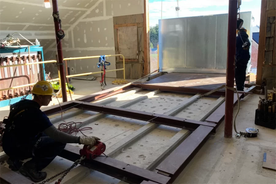 At left, a Cote Corp. rigger operates a pair of winches while a colleague keeps an eye on the HVAC component that's being pulled into the Dana Chemistry Hall attic. (Jacob Kendall/Bates College)