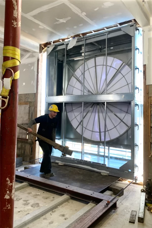 A Cote Corp. rigger wields a jack as the HVAC unit’s enthalpy wheel is tugged into the attic of Dana Chemistry Hall. (Jacob Kendall/Bates College)