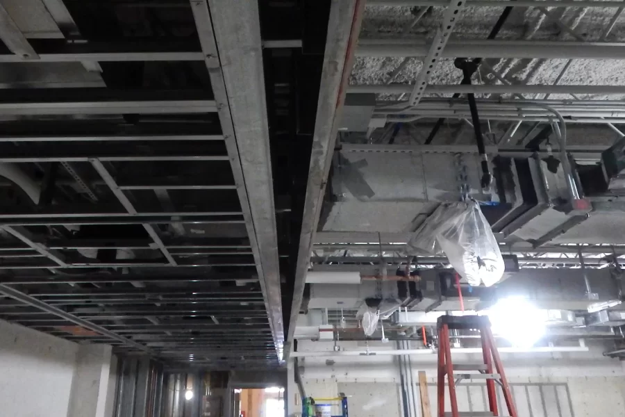 This section of ceiling is divided between two treatments: The left-hand side will be covered with suspended tiles and the right will be left open, with pipes and ducts visible. The fuzzy material at center right is K13, a spray-on acoustic insulation that will also serve as a visual treatment. (Doug Hubley/Bates College)