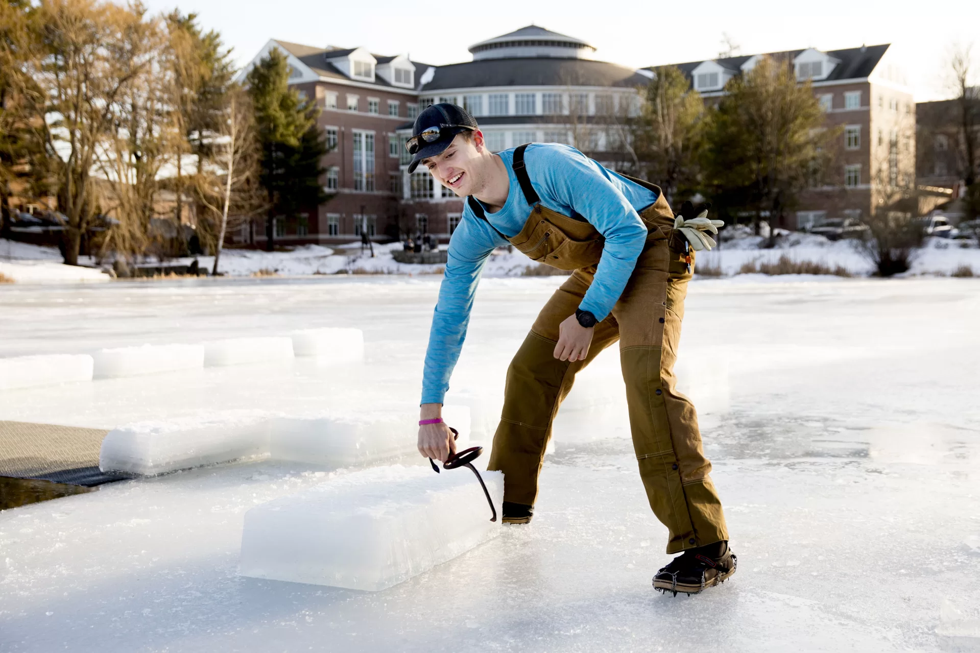 In this 2020 photograph,Jack Fruechte '22 of Minneapolis, Minn., grabs an ice block at Lake Andrews as he and others prepare the hole on Jan. 31 for that year's Puddle Jump. Fruechte cut this year's hole, as he did his first two years, a streak interrupted by the pandemic in 2021. (Phyllis Graber Jensen/Bates College)