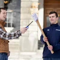 U.S. Rep. Jared Golden ’11 (D-Maine) lights the Winter Carnival torch brandished by Charlie Gainey '24 of Portola Valley, Calif. The torch seemed a little less ornate this year, more of a fuel-soaked rag wrapped around an ax handle. But it got the job done. (Phyllis Graber Jensen/Bates College)