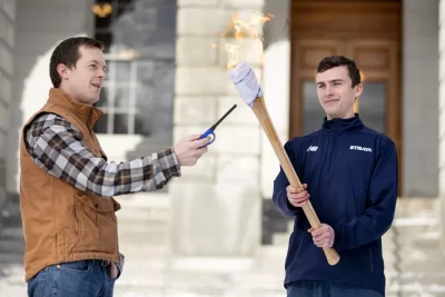 U.S. Rep. Jared Golden ’11 (D-Maine) lights the Winter Carnival torch brandished by Charlie Gainey '24 of Portola Valley, Calif. The torch seemed a little less ornate this year, more of a fuel-soaked rag wrapped around an ax handle. But it got the job done. (Phyllis Graber Jensen/Bates College)