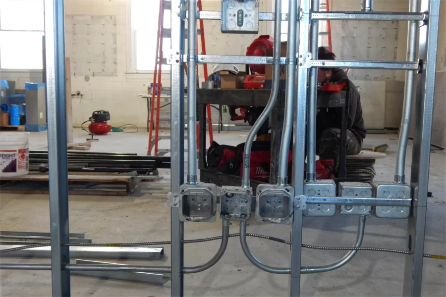 This example of a utility rough-in shows outlet boxes mounted on wall studs separating two third-floor Dana Hall classrooms. An electrician works in the background. (Doug Hubley/Bates College)