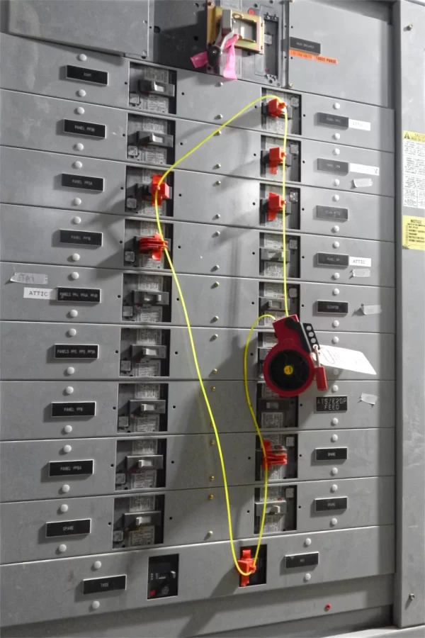 This circuit-breaker panel for Dana’s emergency electricity supply is wearing a lockout-tagout safety system. To protect an electrician working on specific circuits, the breakers with the orange lockouts and the yellow cord can't be turned on. That electrician, whose name is on the paper tag, has the only key for the padlock on the red gizmo that can release the circuits. (Doug Hubley/Bates College)