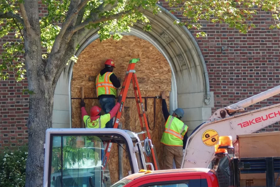 Workers for Gendron & Gendron board up Chase Hall’s main entrance on Campus Aveue prior to the demolition of its concrete stairs. (Doug Hubley/Bates College)