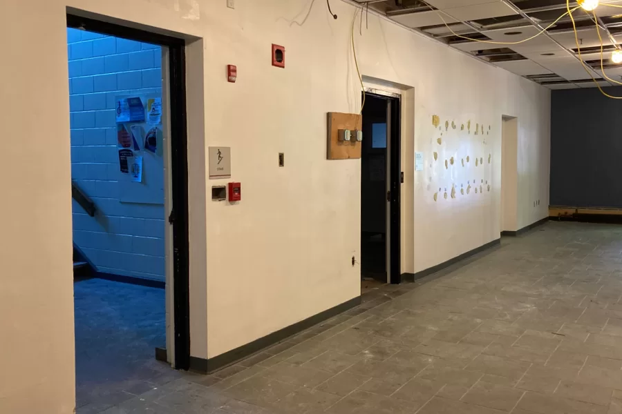 Walls have been stripped, temporary lights and electrical service run in, and some ceiling tiles removed in preparation for extensive demolition in Chase Hall's former main lobby. The door at left leads to Campus Avenue. (Doug Hubley/Bates College)