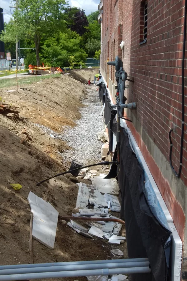 The trench along Chase Hall's Campus Avenue side will facilitate the rebuilding of two entrances. While the foundation is exposed, workers are also applying insulation and waterproofing fabric. (Doug Hubley/Bates College)