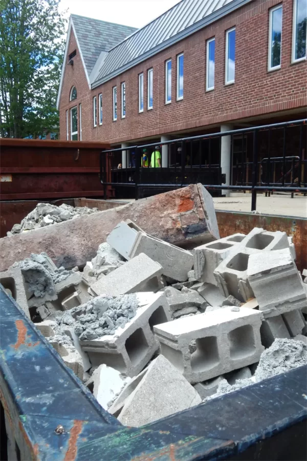 Demolition debris fills a trash container near the Chase Hall loading dock. At center, members of the Chase Hall renovation team are meeting on the dock. (Doug Hubley/Bates College)