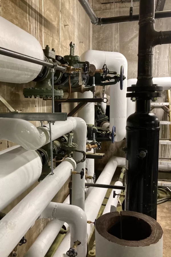 Bare steam-supply pipes that we showed you the other month are now encased in white insulations. The location is the Dana Hall basement where feed lines from the campus-wide steam loop enter. (Doug Hubley/Bates College)
