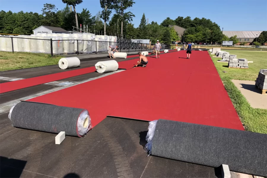 A team from an Illinois company with a great New England name, Wicked Flooring, of Rockford, lays out the new surface on the Russell Street Track on July 28. The concrete blocks will be used to hold the edges of the surface down while glue dries and cooler air causes the Mondo surface to contract. (Jay Burns/Bates College)