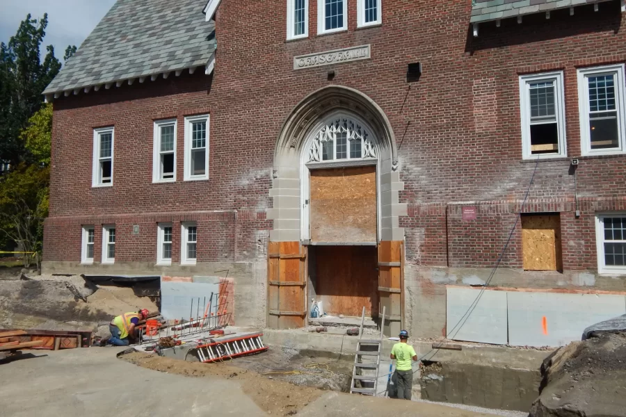 Where people using this Chase Hall entrance previously climbed some steps to enter the building, the renovation will provide an accessible ramp here that descends gently from street level into the ground floor. Here, workers are preparing the site for the new construction. (Doug Hubley/Bates College)