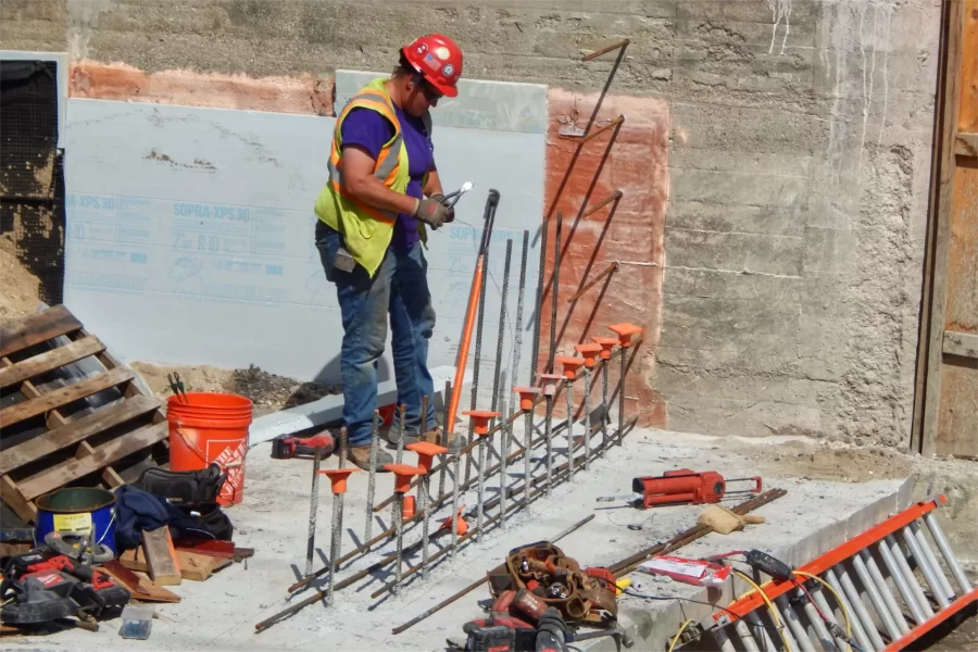 A "rodbuster" wires up rebar in preparation for the placement of a concrete retaining wall at the Chase Hall entrance near the Kenison Gate. (Doug Hubley/Bates College)