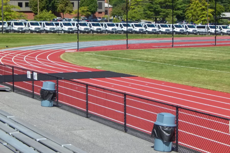 Terracotta is the color of the brand-new Mondo surface on the Russell Street Track. While the surface is settling in, the black mat protects it from foot traffic using the soccer field enclosed by the track. The vans in the background are rented by the college for student activities. (Doug Hubley/Bates College)