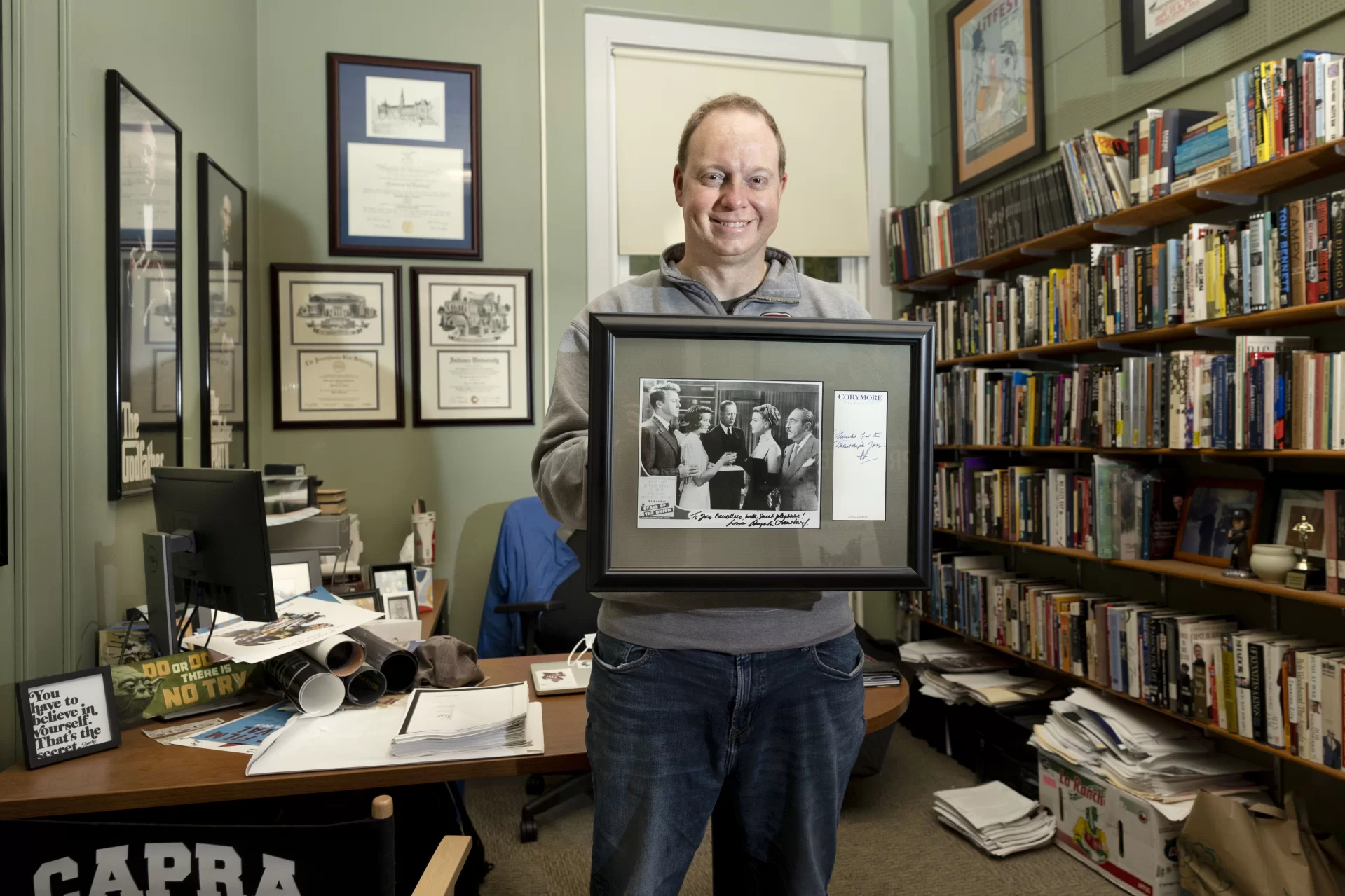 Associate Professor of Rhetoric, Film, and Screen Studies Jon Cavallero poses in his Pettigrew Hall office with his framed photograph and autographs from Angela Lansbury, whom he interviewed by phone for his master’s thesis and inspired him to reach for the stars.