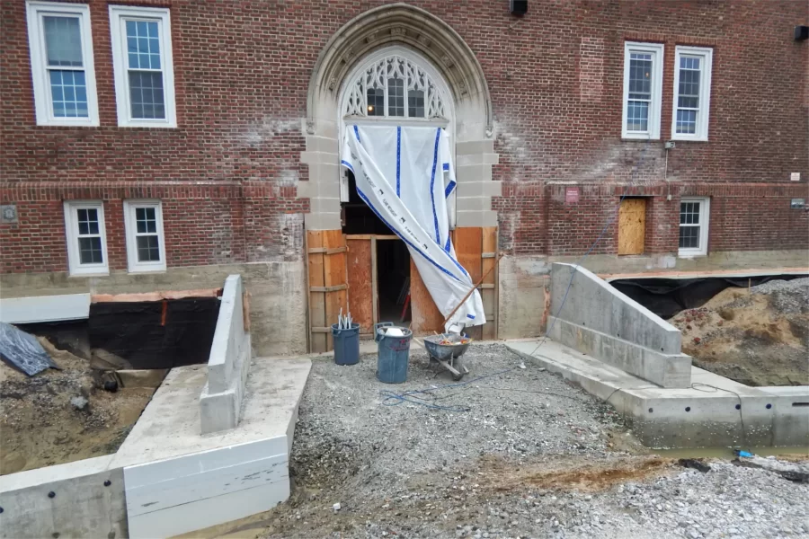 Site work is progressing at the entrance to Chase Hall on Campus Avenue, near Carnegie. The new retaining walls flank the course of a ramp that will lead to a revamped lobby on the ground floor. The wing walls in the foreground will be fronted with built-in concrete benches — an amenity for folks waiting at the bus stop that will return to this spot post-renovation. (Doug Hubley/Bates College)