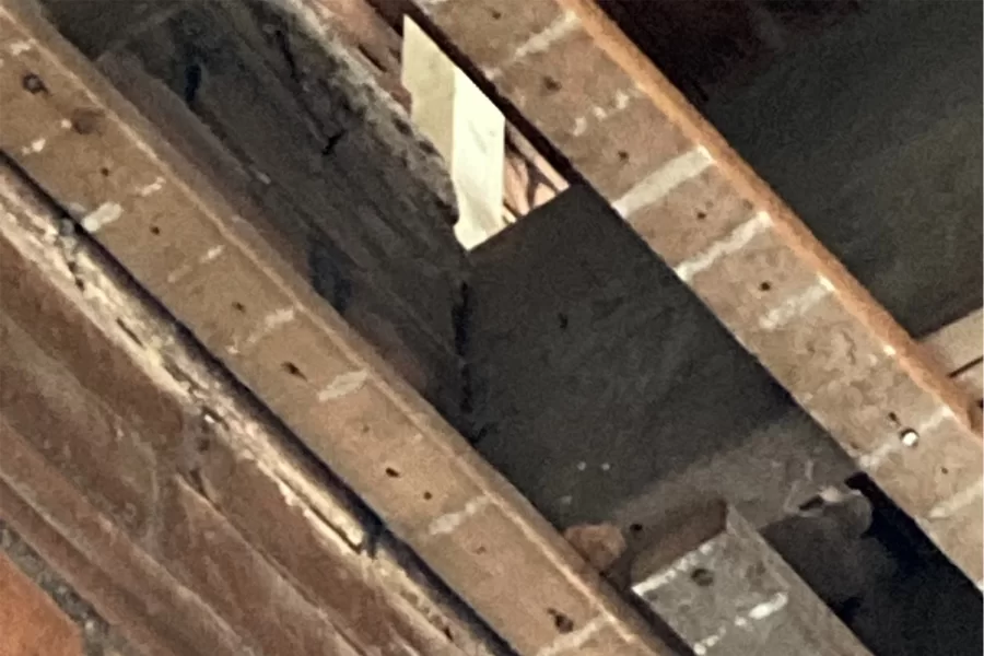Joist right: Seen from below in Chase Hall Lounge, the thick gray wood at center is a joist supporting Chase Hall’s second floor. The joist end rests in a notch, or "pocket,” in the brick wall that helps bear the weight of the floor. Damaged by moisture, other joists had their ends cut off and a different, and less effective, wall attachment installed. The joist joints will be remedied during the current renovation. (Doug Hubley/Bates College)