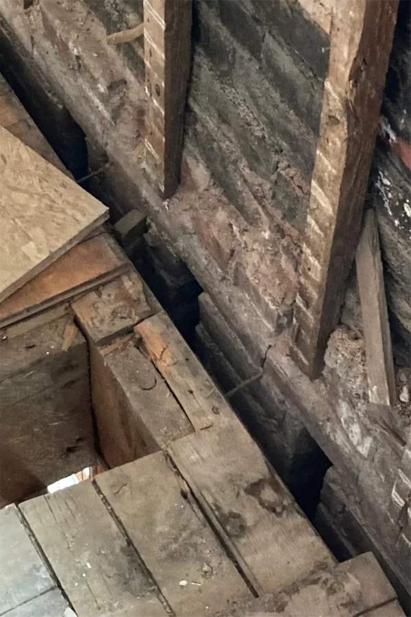 One flight up from the previous photo, empty joist pockets in the brick wall are obvious. The ends of floor joists once rested in those pockets, thereby supporting the floor, but were sawed off because of moisture damage. Called a ledger, the doubled board parallel to the brick was intended to take the weight once borne by the pockets, but hasn't quite been up to the task, causing the second floor to sag. To fix the problem, metal ties that reconnect the joists to the brick will be installed. (Doug Hubley/Bates College)