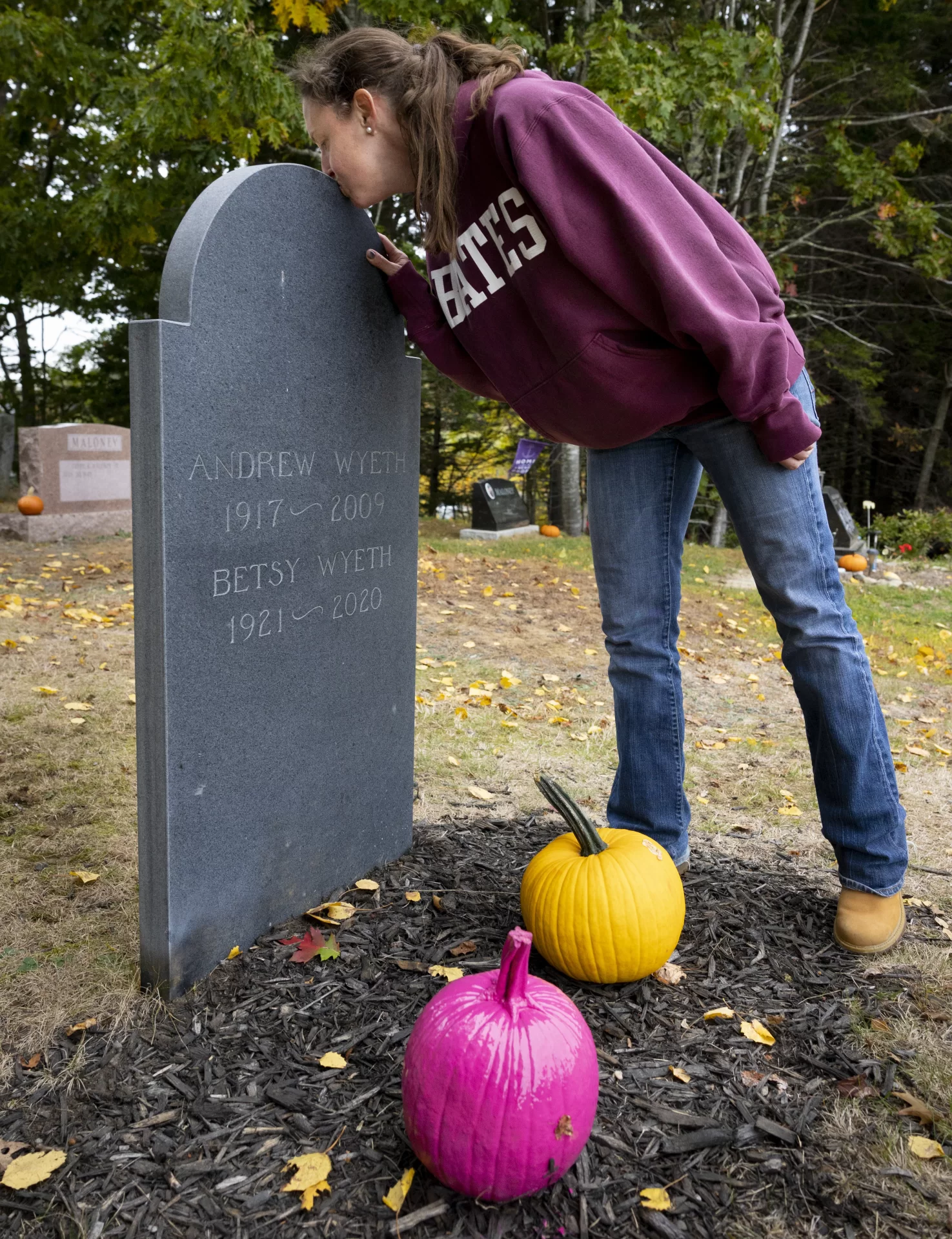 Victoria Wyeth ’01 kisses the gravestone of her grandparents Andrew and Betsy Wyeth, where she left pumpkins, in the spirit of the family's love of Halloween. (Phyllis Graber Jensen/Bates College)