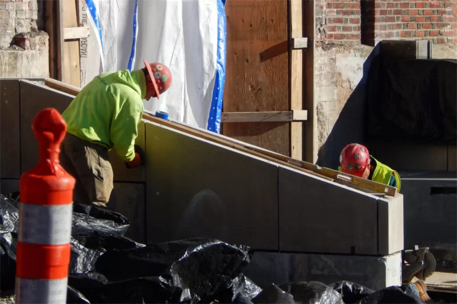 Maine Masonry concrete workers clean the surfaces of a new wall at the Chase Hall entrance on Campus Avenue near the Kenison Gate. (Doug Hubley/Bates College)