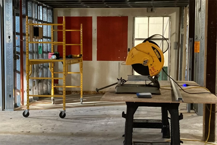 A saw for cutting metal wall studs is set up in the once and future ground-level lobby in Chase Hall. The old post office was situated at left where the new studs are. The red patches are old wall paint that was covered by bulletin boards. (Doug Hubley/Bates College)