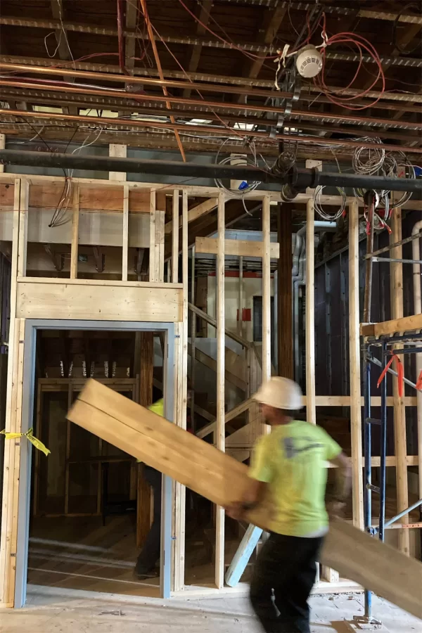 A carpenter carries a board across Chase Hall’s main lobby toward a new stairway going to the second floor. (Doug Hubley/Bates College)