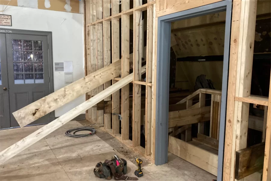 A carpenter passes a plank through the wall studs enclosing this new staircase, which connects the lobby near Chase Hall’s Carnegie Science–facing entrance with the second floor, shown. Note Skelton Lounge at left: It will remain structurally unaltered by the current renovation, but will receive new paint and other cosmetic upgrades. (Doug Hubley/Bates College)