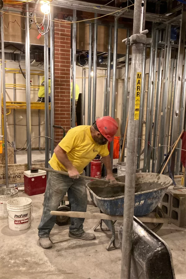 At work in a future Chase Hall meeting room, a mason mixes mortar for a new section of concrete-block wall. Behind him, men are working in what will become the Musicians Union studio. (Doug Hubley/Bates College)