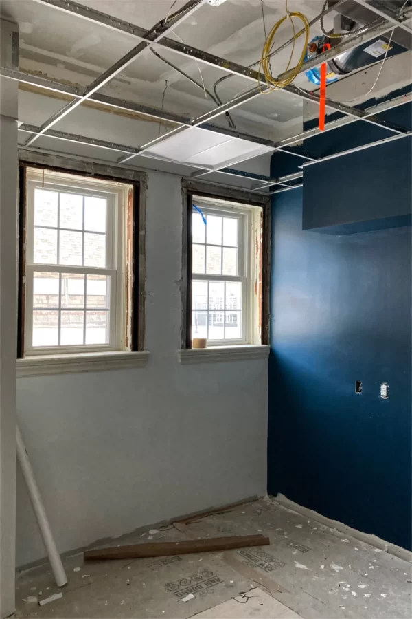 Progress in a second-floor office includes new subflooring, a grid for the suspended ceiling, and the first round of wall paint finish coats. The windows afford a view of Chase Hall’s roof. (Doug Hubley/Bates College)
