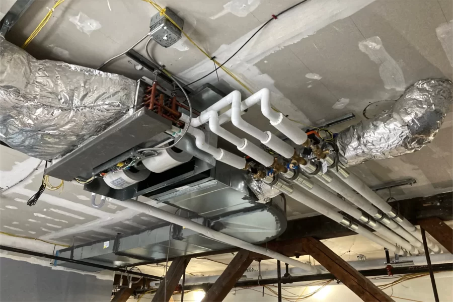 Shown on a second-level ceiling is an HVAC fan-coil unit with air ducts and the white-insulated pipes that feed it hot and cold water. The water heats or cools the air pushed out by the unit. (Doug Hubley/Bates College)