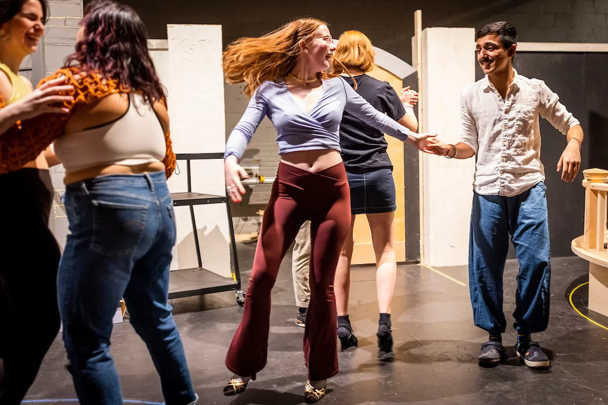 Mia Bernstein ’23 of Bedford, Mass., teaches a dance to actors in Shakespeare’s “Much Ado About Nothing” directed by Assistant Professor of Theater Tim Dugan on the stage of Schaeffer Theatre on Feb. 16, 2023. Stage Manager Lucie Green ’23 of Pittsburgh is also shown in action, seated and moving throughout the theater seats.