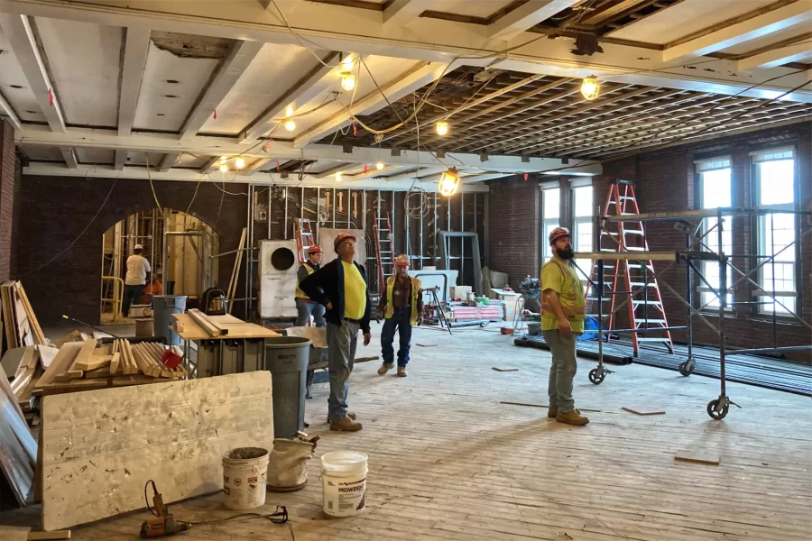 In Chase Hall Lounge, members of the construction team watch a worker outside the photo frame. The current renovation will leave the lounge brighter and expose architectural details that have long been concealed, such as the arched doorway at left rear. (Doug Hubley/Bates College)