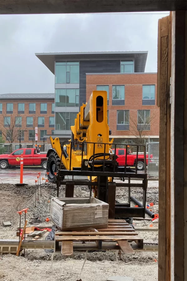 A telescoping-arm forklift operated by Consigli Construction delivers a new mop sink to the Chase Hall entrance near the Kenison Gate. (Doug Hubley/Bates College)